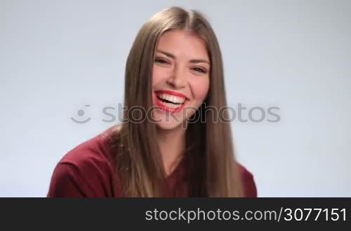 Attractive girl wearing red lipstick, looking at camera, and laughing on white background, showing her white teeth. Cheerful brunette woman in bright positive emotions laughing contagiously.