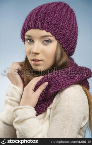 attractive girl with long smooth hair posing with winter clothes, she wearing purple wool hat and scarf and white sweater and looking in camera