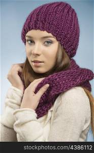attractive girl with long smooth hair posing with winter clothes, she wearing purple wool hat and scarf and white sweater and looking in camera