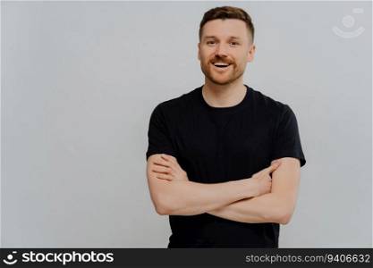 Attractive guy in casual wear, arms crossed, smiling at camera. Positive studio pose.