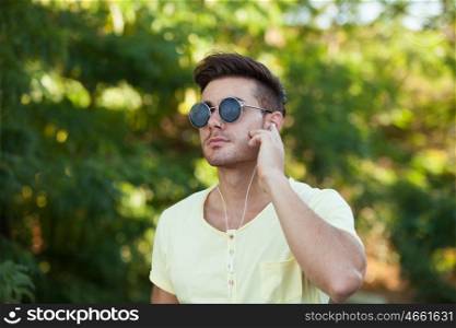 Attractive guy in the park with sunglasses and yellow t-shirt listening music