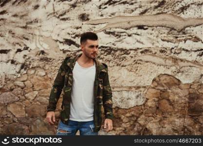 Attractive guy with jacket military stylish on a wall of mud of background