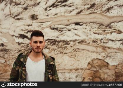 Attractive guy with jacket military stylish on a wall of mud of background