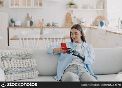 Attractive handicapped woman is texting on smartphone. Disabled european woman browsing internet. Happy girl is holding the phone with bionic artificial arm. Equality and life quality concept.. Handicapped woman is texting on smartphone. Happy girl holding the phone with bionic artificial arm.
