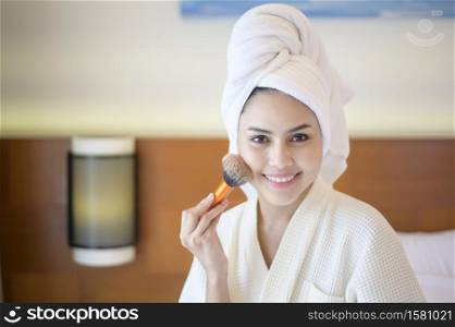 Attractive happy female in white bathrobe is applying natural Make-Up with cosmetic powder brush, Beauty Concept.