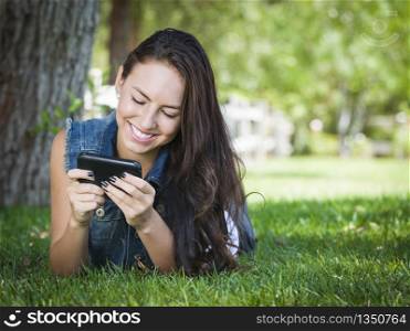 Attractive Happy Mixed Race Young Female Texting on Her Cell Phone Outside Laying in the Grass.