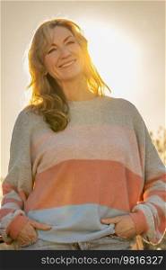 Attractive happy smiling middle aged woman outside back lit by warm sunshine at sunset or sunrise