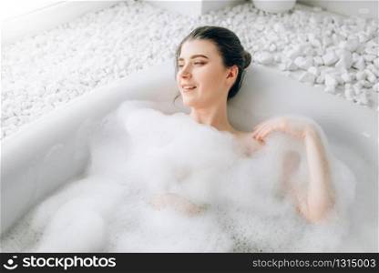 Attractive lady lying in bath with foam, top view. Relaxation, health and skin care in bathroom, spa. Attractive lady lying in bath with foam, top view