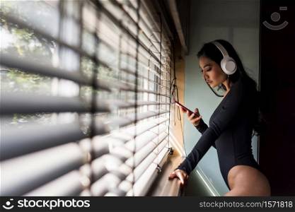 Attractive long hair sexy sensual Asian woman with lingerie headphones play smart phone. listen online streaming music, chat, social media, shopping in living room with natural light through windows.