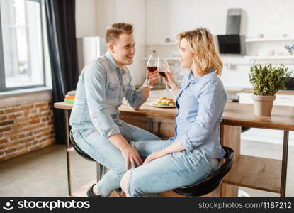 Attractive love couple sitting at the table, romantic dinner. Man and woman drinks wine and eats fruits on the kitchen. Happy lifestyle, beautiful relationship