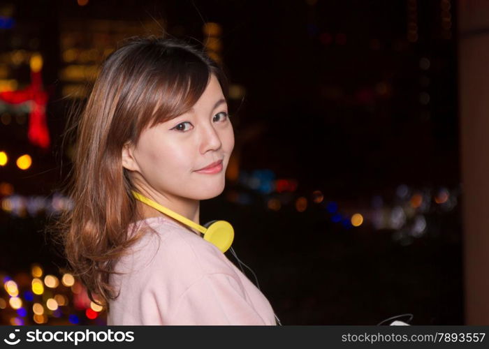 Attractive Malaysian female wearing headphones with city lights in background