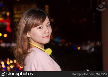 Attractive Malaysian female wearing headphones with city lights in background