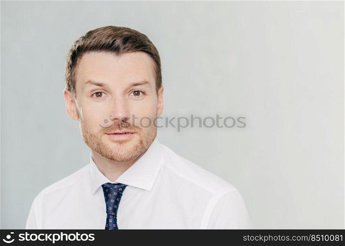 Attractive male freelancer with confident serious expression, works distantly, dressed in elegant white shirt with tie, isolated over white studio wall. People, facial expressions and work concept