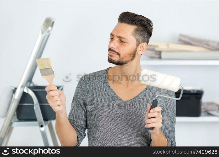 attractive man choosing between paint roller and paint brush