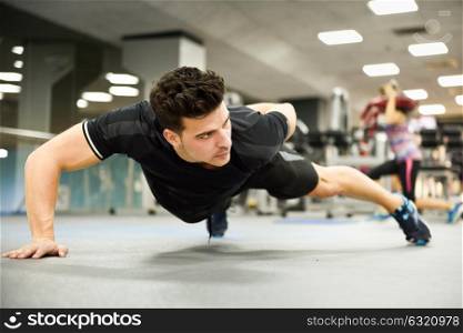 Attractive man doing pushups in the gym. Guy wearing sportwears clothes.