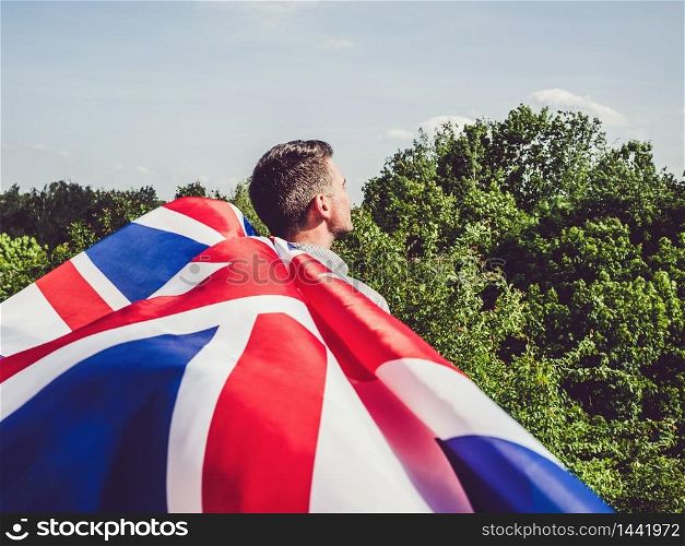 Attractive man holding Australian Flag on blue sky background on a clear, sunny day. View from the back, close-up. National holiday concept. Attractive man holding Australian Flag. National holiday