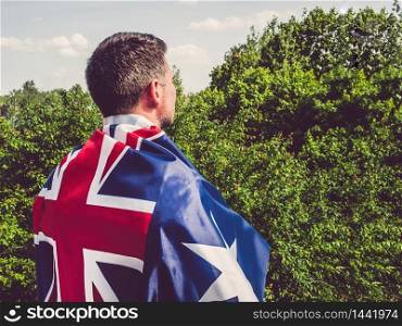 Attractive man holding Australian Flag on blue sky background on a clear, sunny day. View from the back, close-up. National holiday concept. Attractive man holding Australian Flag. National holiday