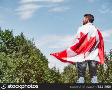 Attractive man holding Canadian Flag on blue sky background on a clear, sunny day. View from the back, close-up. National holiday concept. Attractive man holding Canadian Flag. National holiday