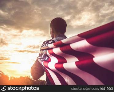Attractive man holding Flag of the United States on blue sky background on a clear, sunny day. View from the back, close-up. National holiday concept. Attractive man holding Flag of the United States