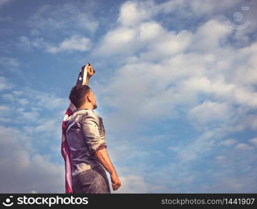 Attractive man holding Flag of the United States on blue sky background on a clear, sunny day. View from the back, close-up. National holiday concept. Attractive man holding Flag of the United States