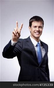 Attractive man in a suit shows a sign of &acute;peace&acute; on a gray background
