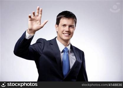 Attractive man in a suit with his hand raised on a gray background