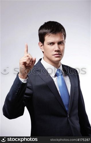 Attractive man in a suit with the index finger up on a gray background