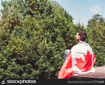 Attractive man in jeans and denim shirt holding a Canadian Flag against a clear, sunny, blue sky. View from the back, close-up. National holiday concept. Man holding a Canadian Flag. National holiday