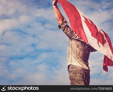 Attractive man in jeans and denim shirt waving a Canadian Flag against a clear, sunny, blue sky. View from the back, close-up. National holiday concept. Man waving a Canadian Flag. National holiday