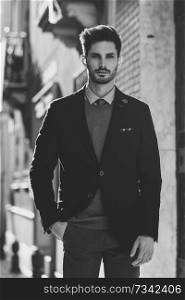 Attractive man in the street wearing british elegant suit. Young bearded businessman with modern hairstyle in urban background. Black and white photograph.. Attractive man wearing british elegant suit in the street. Modern hairstyle.
