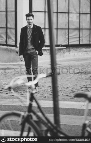 Attractive man in the street wearing british elegant suit near a vintage bicycle. Young bearded businessman with modern hairstyle in urban background.