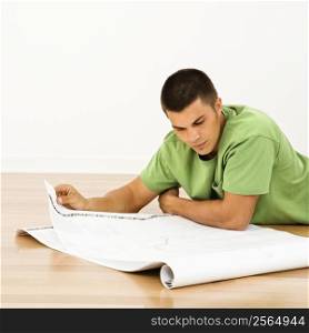 Attractive man lying on floor in home reading house plans.