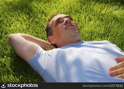 Attractive man lying on green grass in a park relaxing