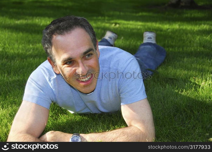 Attractive man lying on green grass in a park relaxing