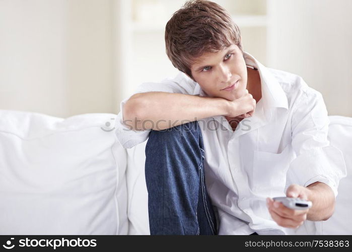 Attractive man on the couch switches remote control TV channels