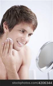 Attractive man rubs the lotion face in the mirror