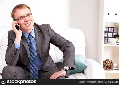 Attractive man sitting on sofa and speaking on the telephone in living room