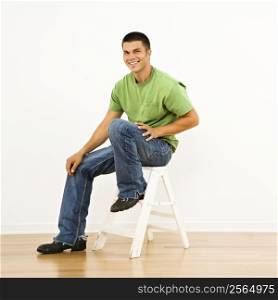 Attractive man sitting on stepladder in home smiling.