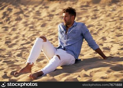 Attractive man sitting on the sand of the beach looking at the horizon.. Attractive man sitting on the sand of the beach