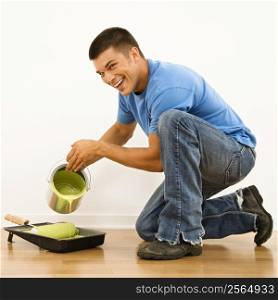 Attractive man smiling and pouring paint into roller pan in home.