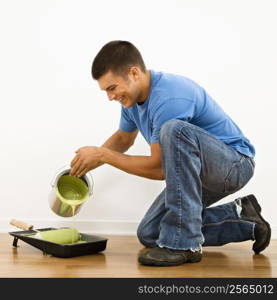 Attractive man smiling and pouring paint into roller pan in home.