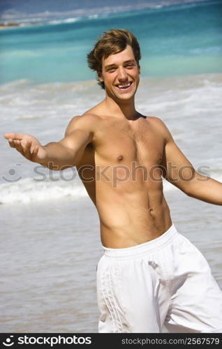 Attractive man walking on Maui, Hawaii beach smiling and reaching out.