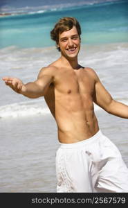 Attractive man walking on Maui, Hawaii beach smiling and reaching out.