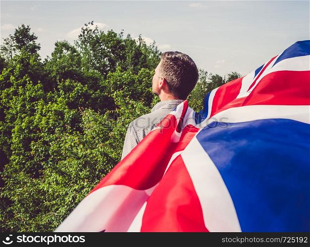 Attractive man waving a British Flag against a background of trees and blue sky. View from the back, close-up. National holiday concept. Bright, fruit ice cream on a vintage plate