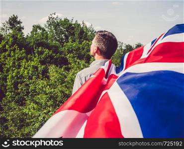 Attractive man waving a British Flag against a background of trees and blue sky. View from the back, close-up. National holiday concept. Bright, fruit ice cream on a vintage plate