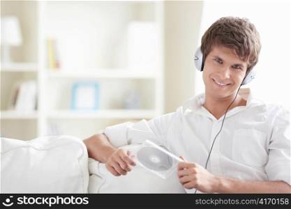 Attractive man with a disk in his hands listening to music through headphones on the sofa