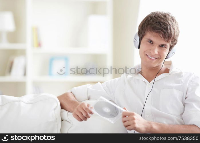 Attractive man with a disk in his hands listening to music through headphones on the sofa