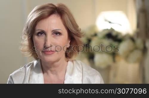 Attractive mature woman smiling. Facial expression of happy elderly lady smiling and looking at camera. Close up view.