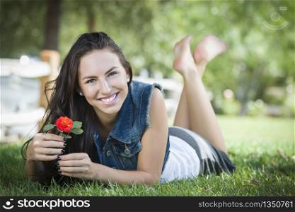 Attractive Mixed Race Girl Portrait Laying in Grass Outdoors with Flower.