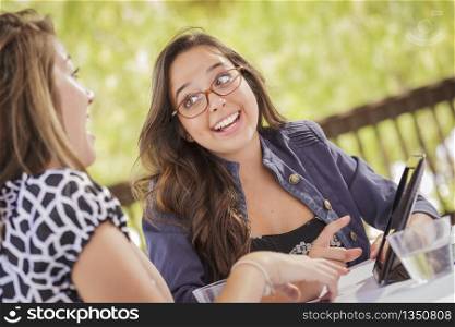 Attractive Mixed Race Girls Smiling and Talking While Working on Tablet Computer Sitting Outdoors.